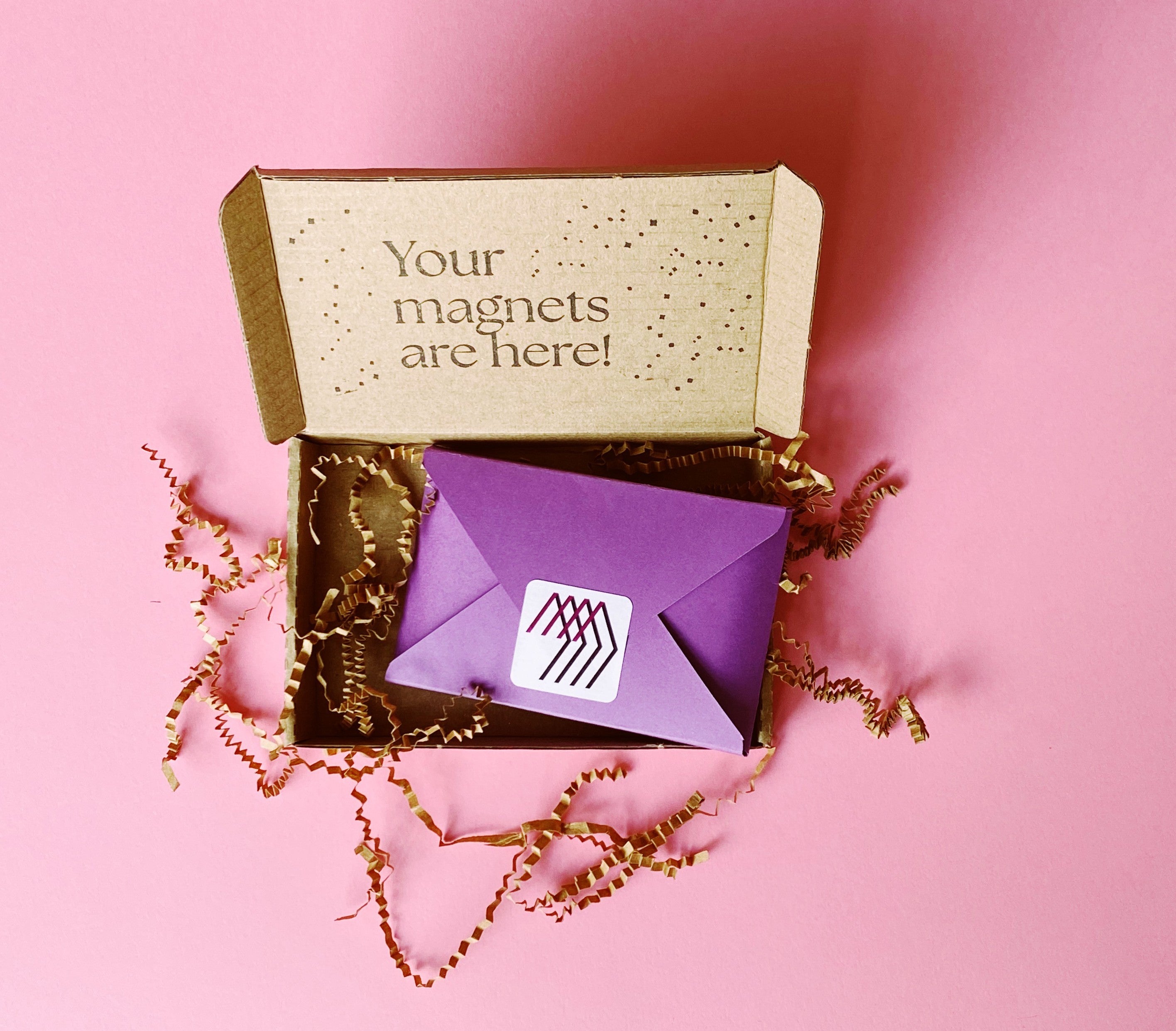 Magnetic Love shipping box on a pink background, containing personalized photo magnets wrapped in kraft paper.